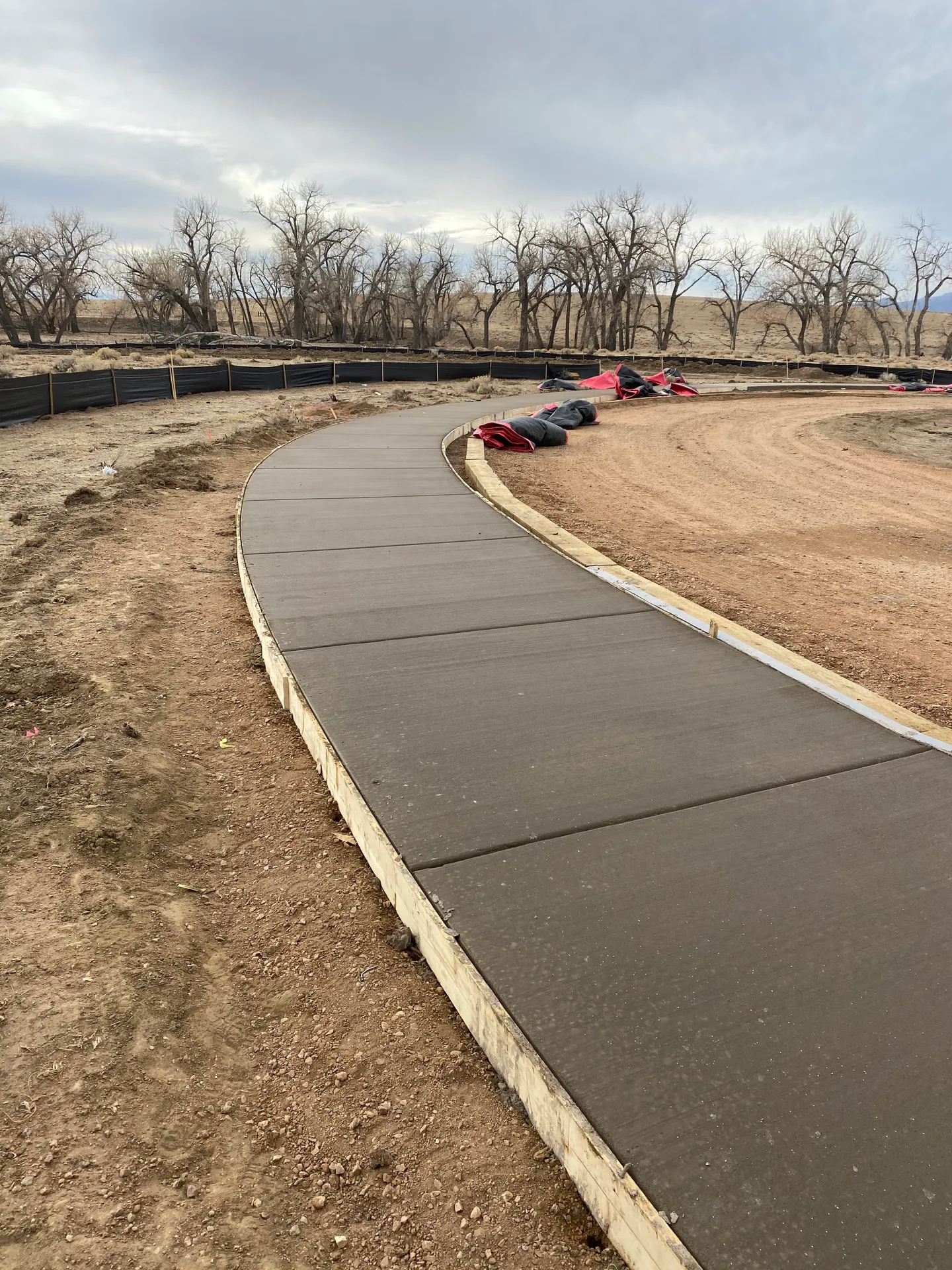 Curved concrete walkway with wood forms still set across an open Colorado job site