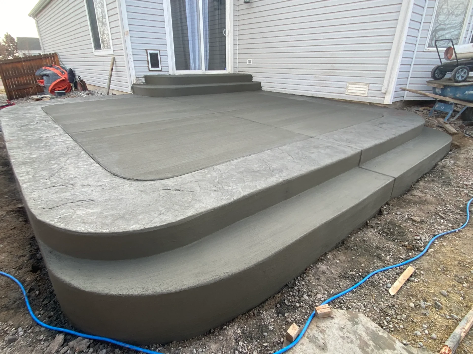 Raised broom-finish concrete patio with stamped border and wrap-around steps behind a Colorado Springs home