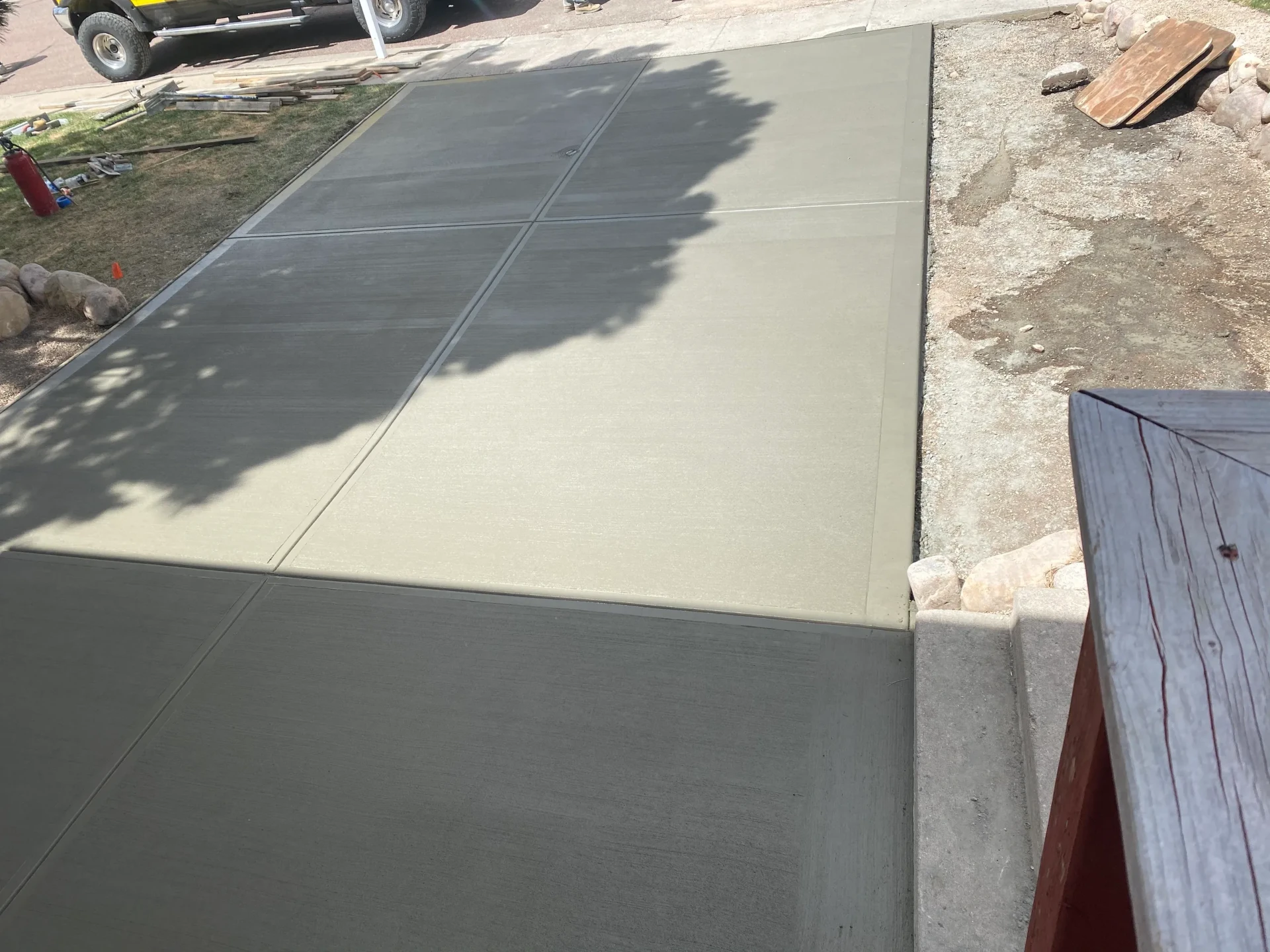 New broom-finished concrete driveway apron and sidewalk beside rock landscaping in Colorado Springs, CO