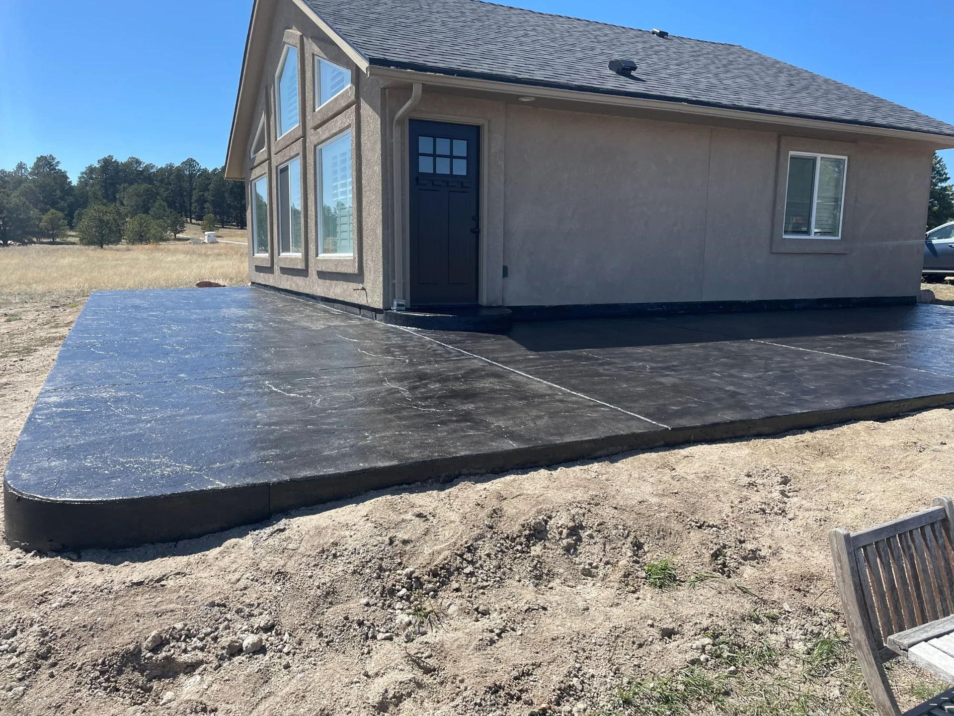 Dark charcoal stamped concrete patio wrapping a stucco home on a Colorado acreage