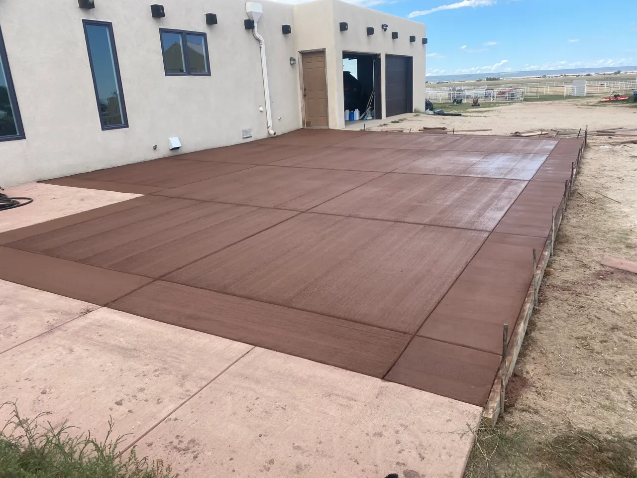 Large brown colored broom-finish concrete patio slab behind a stucco home in Yoder, CO