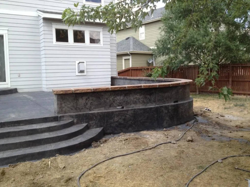 Charcoal stamped concrete patio with curved steps and retaining seat wall in El Paso County, CO